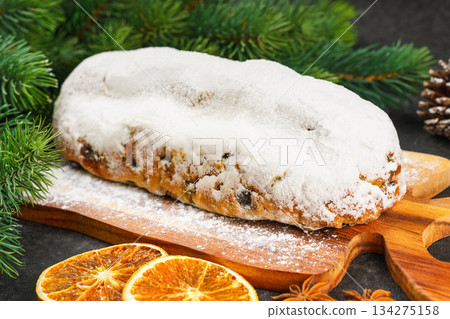 Traditional Christmas Stollen, sweet fruit loaf with sugar icing on wooden board and festive decor 134275158