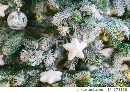 Christmas tree snow with white star ornament on frosted green branches with festive holiday lights Christmas tree snow with white star ornament on frosted green branches with festive holiday lights 134275186