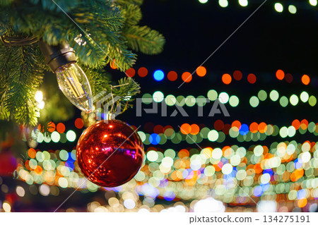 Christmas tree branch decorated with shiny red ball on glowing festive holiday lights background Christmas tree branch decorated with shiny red ball on glowing festive holiday lights background 134275191