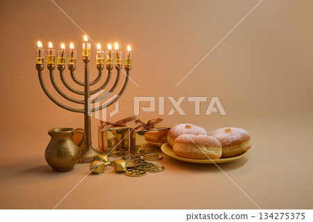 Hanukkah Celebration Setup. A menorah, dreidels, gift boxes, and donuts on a beige background Hanukkah Celebration Setup. A menorah, dreidels, gift boxes, and donuts on a beige background 134275375