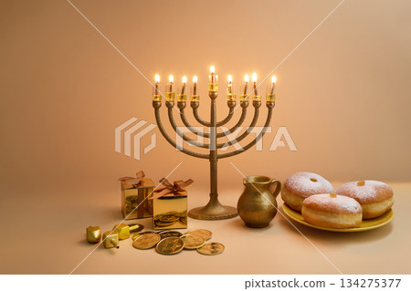 Hanukkah Celebration Setup. A menorah, dreidels, gift boxes, and donuts on a beige background 134275377