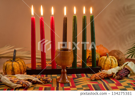 Kwanzaa Celebration Setup. A vibrant Kwanzaa display with colorful candles, fruits, corn, and a wooden chalice Kwanzaa Celebration Setup. A vibrant Kwanzaa display with colorful candles, fruits, corn, and a wooden chalice 134275381
