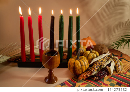 Kwanzaa Celebration Setting. Warm Kwanzaa scene with lit candles, harvest vegetables, and a wooden chalice Kwanzaa Celebration Setting. Warm Kwanzaa scene with lit candles, harvest vegetables, and a wooden chalice 134275382