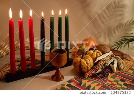Kwanzaa Celebration Setting. Warm Kwanzaa scene with lit candles, harvest vegetables, and a wooden chalice Kwanzaa Celebration Setting. Warm Kwanzaa scene with lit candles, harvest vegetables, and a wooden chalice 134275383