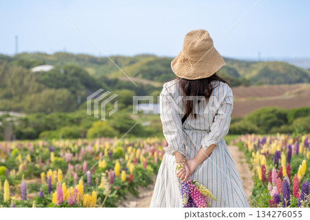一位年輕女子戴著草帽，身穿連身裙，背對著鏡頭，走過一片花田。 134276055