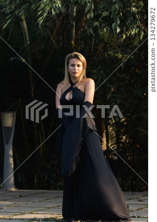 A beautiful Caucasian blonde is walking in nature wearing a black dress. The luxury of the territory of an expensive hotel. A beautiful Caucasian blonde is walking in nature wearing a black dress. The luxury of the territory of an expensive hotel. 134279672