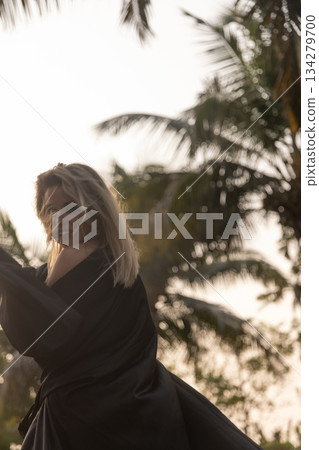 A beautiful Caucasian blonde is walking in nature wearing a black hat. The luxury of the territory of an expensive hotel. 134279700