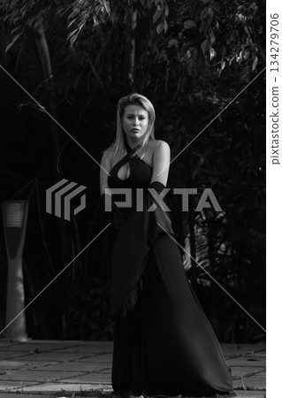 A beautiful Caucasian blonde is walking in nature wearing a black dress. The luxury of the territory of an expensive hotel. A beautiful Caucasian blonde is walking in nature wearing a black dress. The luxury of the territory of an expensive hotel. 134279706