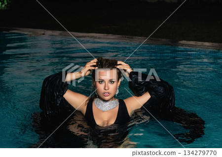 A sexy girl in a black swimsuit poses at night by the pool at a party.  134279770