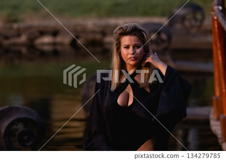 A beautiful Caucasian blonde is walking in nature wearing a black hat.  134279785