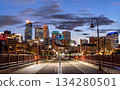 Night view from Stone Arch Bridge features Minneapolis skyline and Mississippi River. Illuminated walking path leads to downtown skyscrapers under blue sky 134280501