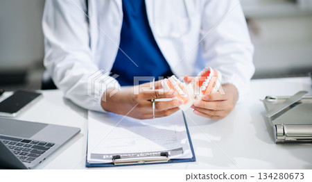 Dentist sitting at table with jaw samples tooth model and working with tablet and laptop. professional dental clinic. 134280673