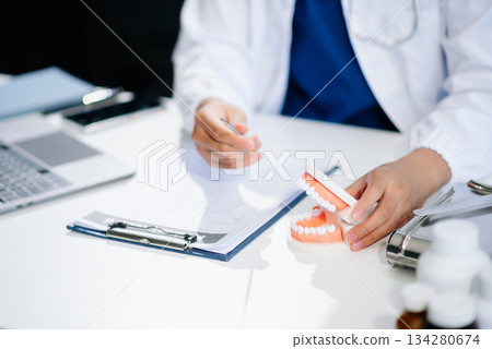 Dentist sitting at table with jaw samples tooth model and working with tablet and laptop. professional dental clinic. Dentist sitting at table with jaw samples tooth model and working with tablet and laptop. professional dental clinic. 134280674