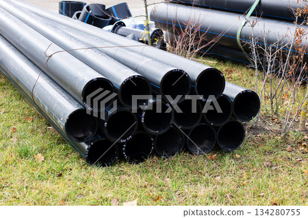 Grasscovered outdoor area featuring stacked black plastic pipes illuminated by early sunlight 134280755