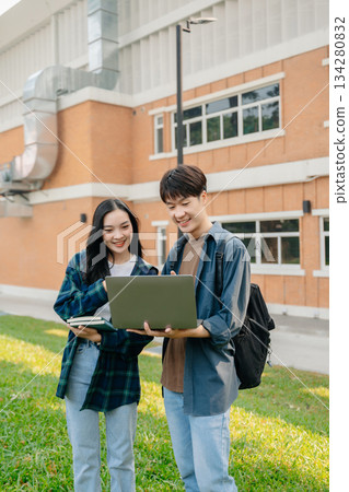 Two smart young Asian college students focusing on his school project, looking at laptop and tablet, discussing and working together 134280832