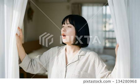 清晨，一位女子拉開窗簾，沐浴在陽光下。 134280968