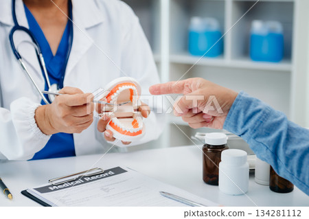 Concentrated dentist sitting at table with jaw samples tooth model and working with tablet and laptop in dental office professional dental clinic. medical doctor working 134281112