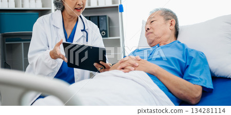 Asian doctor in white suit take notes while discussing and Asian elderly, man patient who lying on bed with receiving saline solution 134281114