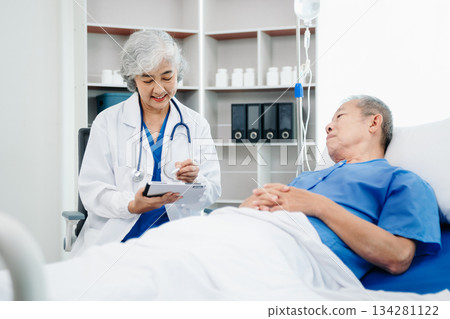 Asian doctor in white suit take notes while discussing and Asian elderly, man patient who lying on bed with receiving saline solution 134281122
