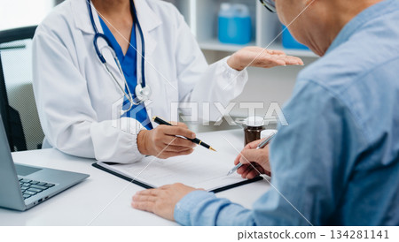 A professional physician talks to discuss results or symptoms and gives a recommendation to a male patient and signs a medical paper 134281141