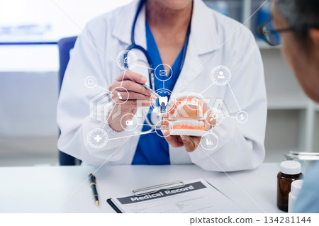 Concentrated dentist sitting at table with jaw samples tooth model and working with tablet and laptop in dental office professional dental clinic. medical doctor working 134281144