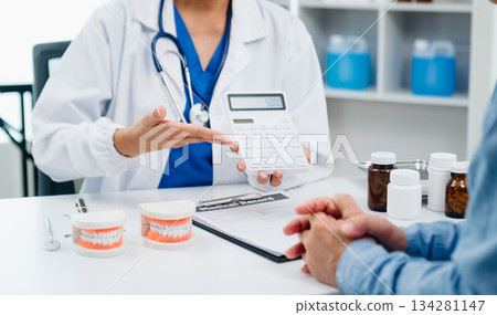 Concentrated dentist sitting at table with jaw samples tooth model and working with tablet and laptop in dental office professional dental clinic. medical doctor working Concentrated dentist sitting at table with jaw samples tooth model and working with tablet and laptop in dental office professional dental clinic. medical doctor working 134281147