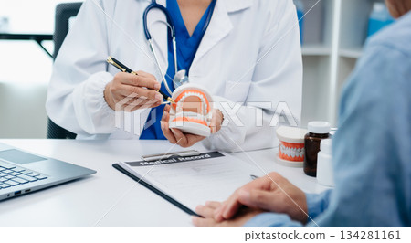 Concentrated dentist sitting at table with jaw samples tooth model and working with tablet and laptop in dental office professional dental clinic. medical doctor working 134281161