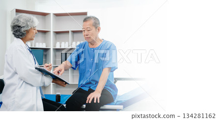 Asian doctor in white suit take notes while discussing and Asian elderly, man patient who lying on bed with receiving saline solution 134281162