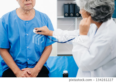 Asian doctor in white suit take notes while discussing and Asian elderly, man patient who lying on bed with receiving saline solution Asian doctor in white suit take notes while discussing and Asian elderly, man patient who lying on bed with receiving saline solution 134281227