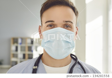 Young man doctor wearing medical mask with stethoscope looking at camera in clinic. Young man doctor wearing medical mask with stethoscope looking at camera in clinic. 134281558