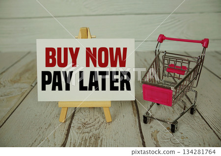 Buy Now Pay Later text on paper card and trolley shopping cart on wooden background Buy Now Pay Later text on paper card and trolley shopping cart on wooden background 134281764