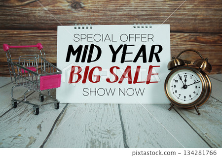 Mid Year Big Sale Shop Now Special Offer text on paper card with alarm clock and trolley shopping cart on wooden background Mid Year Big Sale Shop Now Special Offer text on paper card with alarm clock and trolley shopping cart on wooden background 134281766