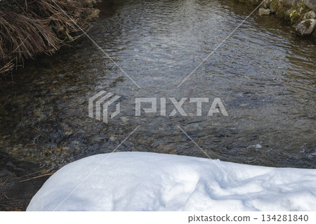 A clear river with snow edges and pebbles visible A clear river with snow edges and pebbles visible 134281840
