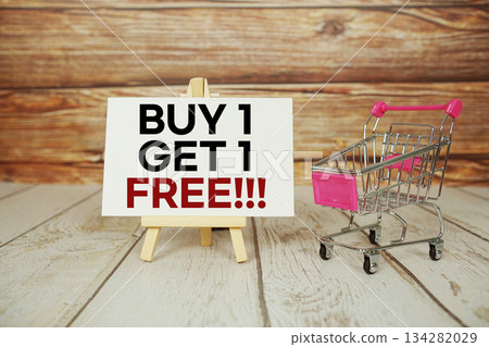 Buy 1 Get 1 Free!!! on sign board with Mini Shopping Cart on Wooden Background Buy 1 Get 1 Free!!! on sign board with Mini Shopping Cart on Wooden Background 134282029