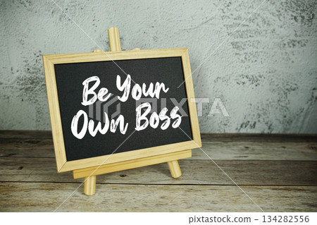 wooden easel displays a blackboard with the bold white text "Be Your Own Boss" set against a rustic wooden surface and textured gray wall background wooden easel displays a blackboard with the bold white text "Be Your Own Boss" set against a rustic wooden surface and textured gray wall background 134282556