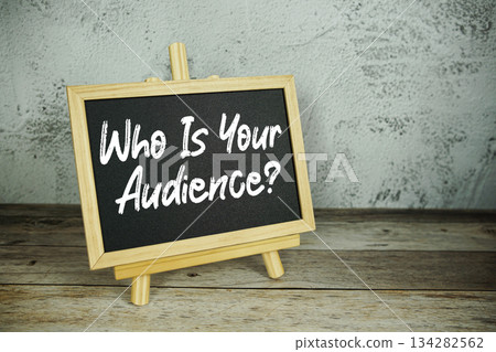 wooden easel displays a blackboard with the bold white text "Who Is Your Audience?" set against a rustic wooden surface and textured gray wall background wooden easel displays a blackboard with the bold white text "Who Is Your Audience?" set against a rustic wooden surface and textured gray wall background 134282562