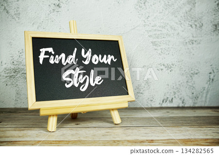wooden easel displays a blackboard with the bold white text "Find Your Style" set against a rustic wooden surface and textured gray wall background 134282565