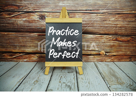 wooden easel holds a blackboard with the white text "Practice Makes Perfect" set against a rustic wooden wall and light-colored wooden floor wooden easel holds a blackboard with the white text "Practice Makes Perfect" set against a rustic wooden wall and light-colored wooden floor 134282578