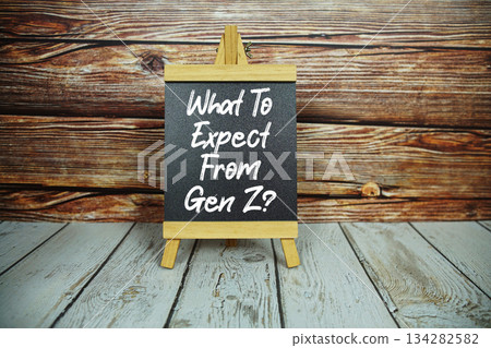 wooden easel holds a blackboard with the white text "What To Expect From Gen Z" set against a rustic wooden wall and light-colored wooden floor 134282582