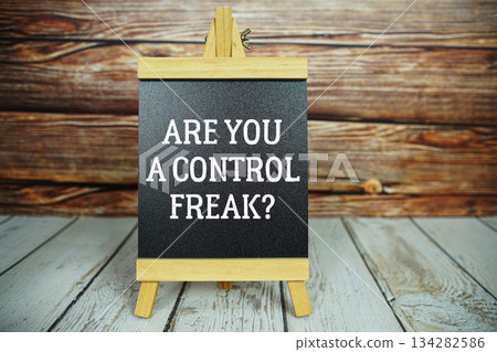 wooden easel holds a blackboard with the white text "Are You a Control Freak?" set against a rustic wooden wall and light-colored wooden floor wooden easel holds a blackboard with the white text "Are You a Control Freak?" set against a rustic wooden wall and light-colored wooden floor 134282586