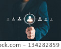 Businessman holding magnifying glass focusing on candidate icon, symbolizing recruitment, human resources, employee selection, target audience, and business hiring strategy. 134282859