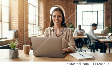 一位女士在共享辦公空間使用筆記型電腦，並對鏡頭微笑。 134283593