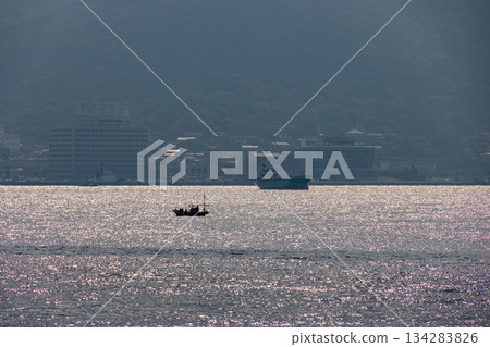 一艘漁船漂浮在海面上，沐浴在陽光下，遠處有一艘大船。 134283826