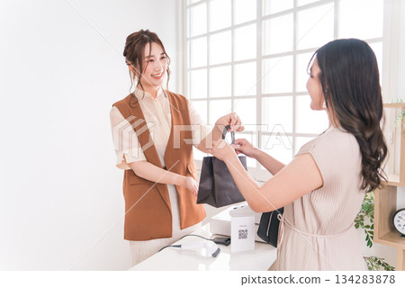 服飾店/雜貨店的收銀台上,店員遞出商品,女顧客收到商品。 服飾店/雜貨店的收銀台上,店員遞出商品,女顧客收到商品。 134283878