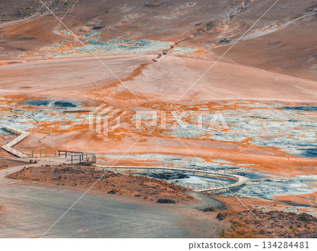 Vibrant orange and blue geothermal landscape in Iceland featuring steaming vents, mud pots, and wooden walkways for safe exploration. 134284481