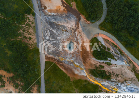 Aerial image of a geothermal Strokkur Geyser in Iceland featuring a hot spring, colorful mineral deposits, green vegetation, a road, and pathways. 134284515