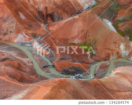 Vibrant rhyolite hills of Kerlingarfjoll with red, orange, and green hues, geothermal streams, a wooden bridge, and visible hiking trails. 134284574