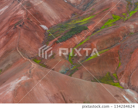 Multicolored rhyolite hills of Iceland's Rainbow Mountains, featuring red, orange, and green hues, with a winding path through the rugged terrain. 134284624