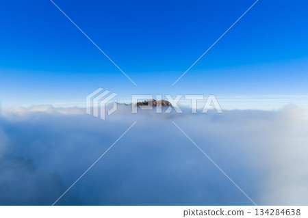A lone rocky peak rises through a cloud inversion on Madeira Island, Pico do Arieiro, Portugal. Soft daylight illuminates the crest, wide negative space and centered horizon suggest early hours. A lone rocky peak rises through a cloud inversion on Madeira Island, Pico do Arieiro, Portugal. Soft daylight illuminates the crest, wide negative space and centered horizon suggest early hours. 134284638