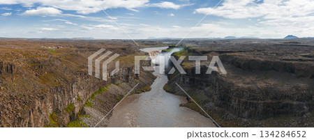 Dettifoss waterfall in Iceland cascades into a rugged canyon, surrounded by basalt cliffs, rocky terrain, green patches, and mist under a cloudy sky. Dettifoss waterfall in Iceland cascades into a rugged canyon, surrounded by basalt cliffs, rocky terrain, green patches, and mist under a cloudy sky. 134284652